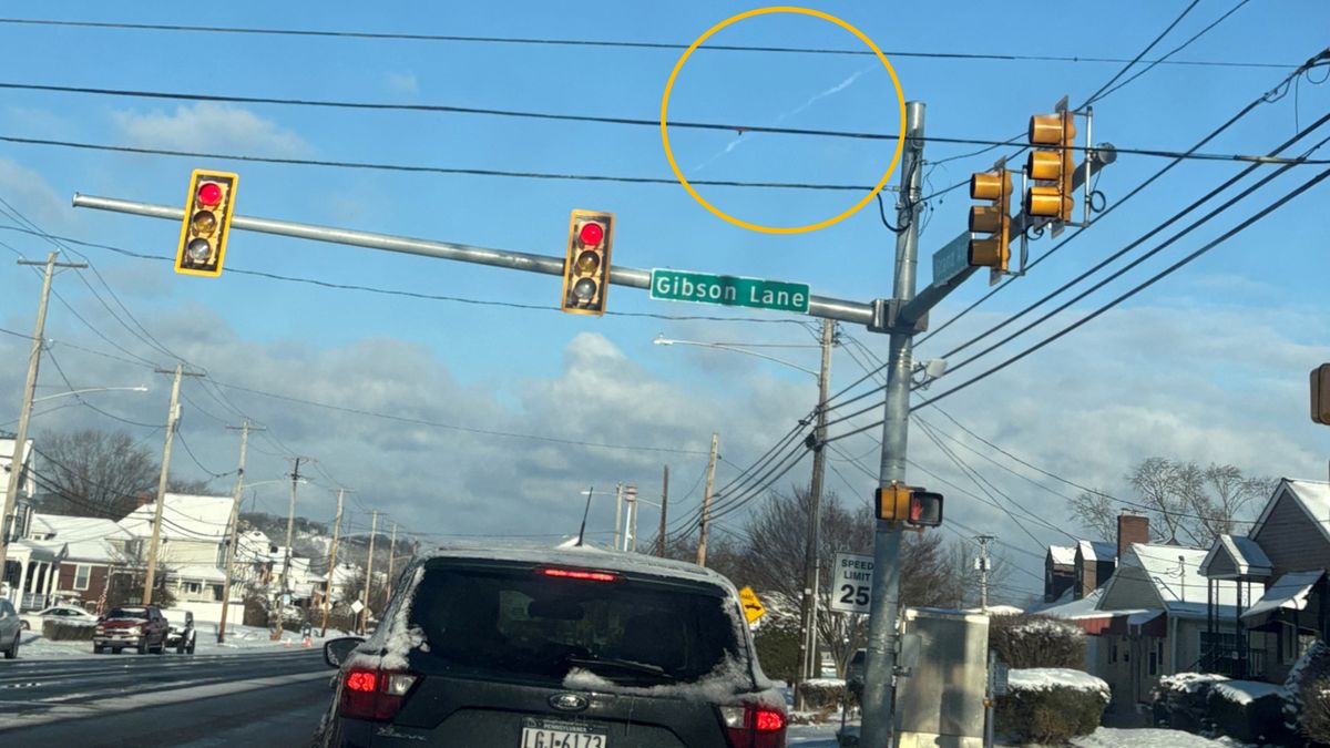 Photo of a car on road with a meteor streaking through the daytime sky (circled)