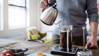 A man pouring from a silver kettle into a French press