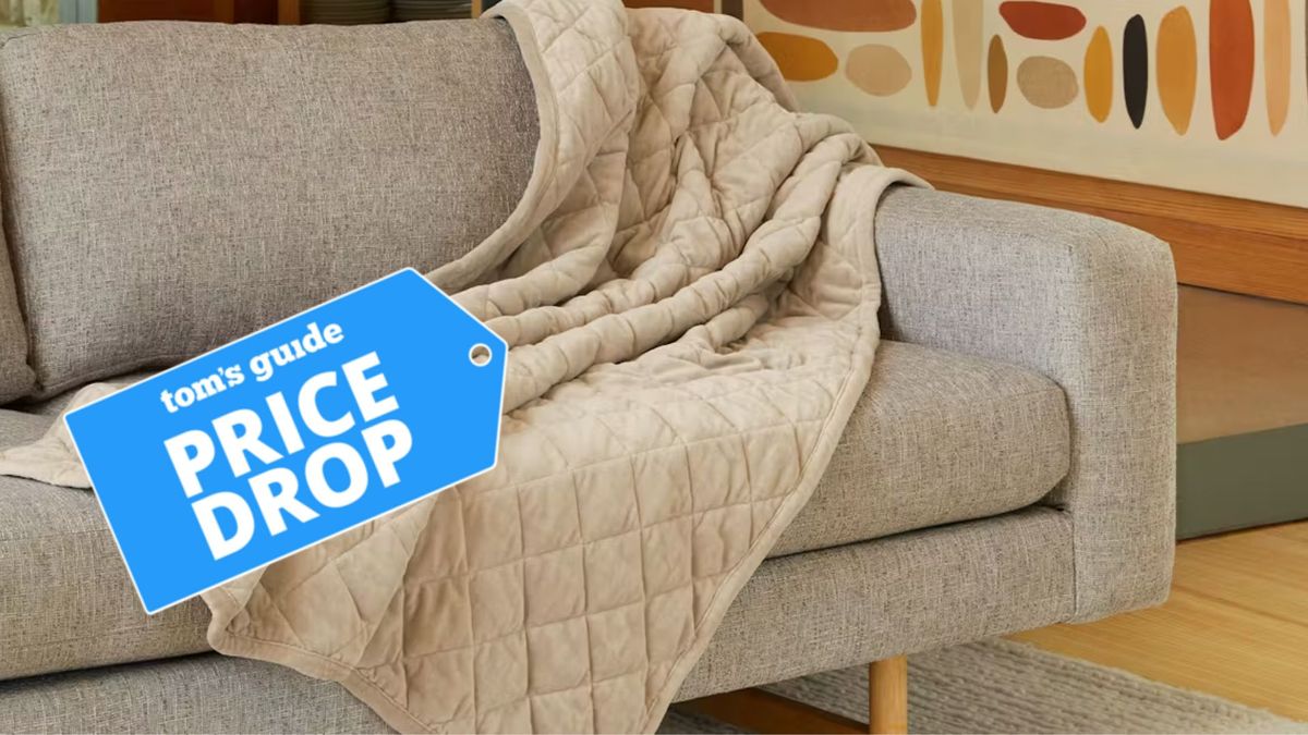 The image shows a beige Saatva weighted blanket draped over a grey sofa