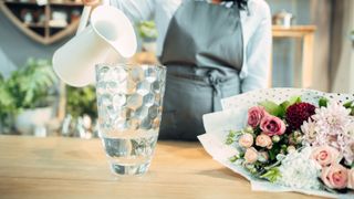 A pitcher pouring water into a vase next to a bouquet of flowers