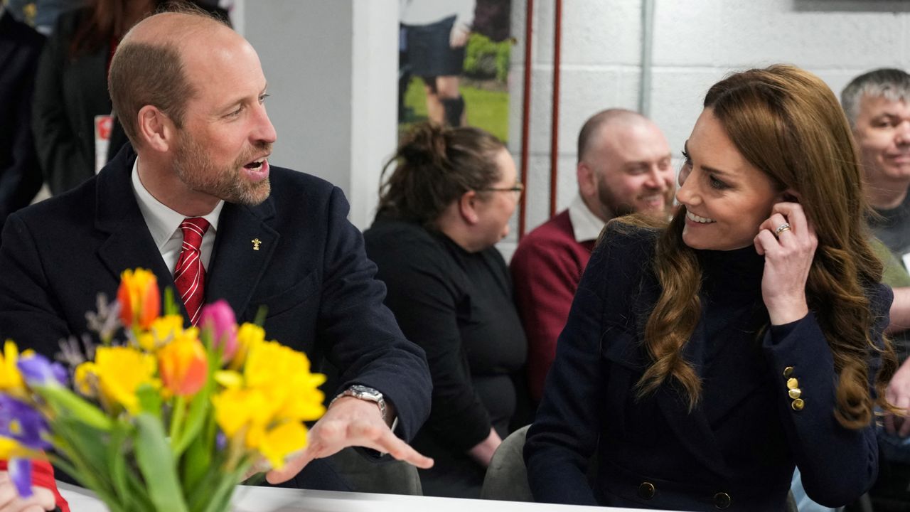 Prince William and Kate Middleton sitting at a white table smiling at each other during the Six Nations Rugby game