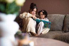 Happy mother and daughter in pyjamas sitting on sofa at home and reading a book.