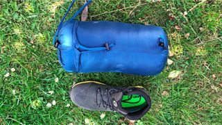Alpkit Pipedream 400 sleeping bag packed in its double compression bag bag, next to a walking boot for comparison