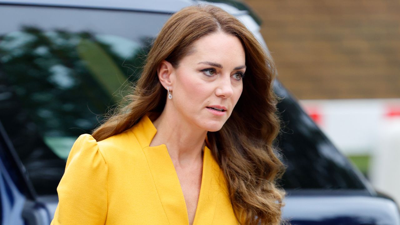 Kate Middleton has long, wavy brunette hair and wears a bright yellow dress with puffy sleeves