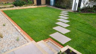 A freshly laid turf lawn in a small garden with stepping stone paving set diagonally across the new lawn creating a walkway