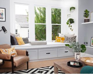 A living room with grey bespoke window seat nook, geometric black and white monochrome rug decor and tan leather armchair