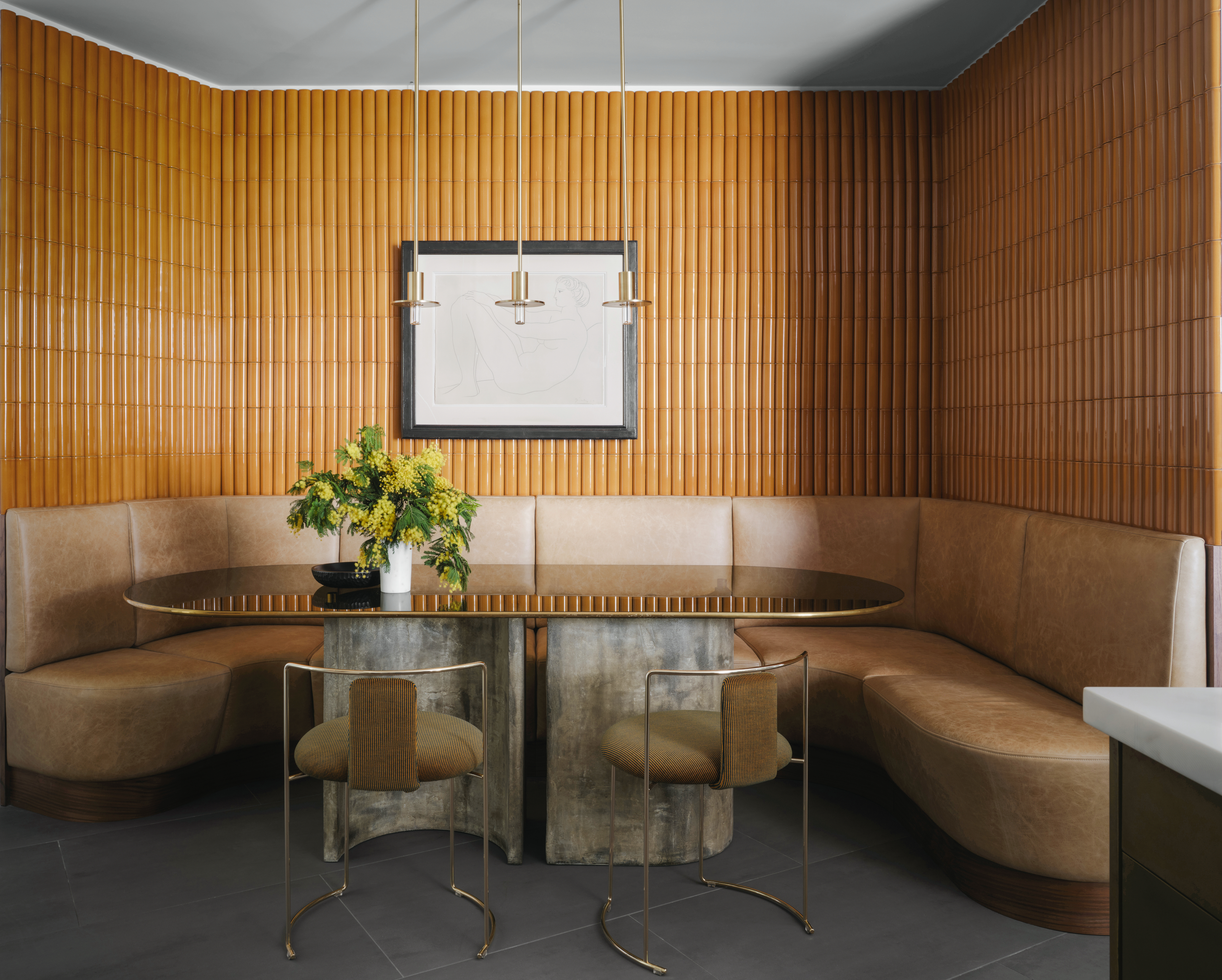 Breakfast nook with beige leather banquette seating, metallic-topped dining table, ochre finger tiles on walls and three pendant lights overhead