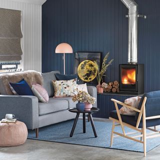 Living room with blue panelled feature wall behind a wood burner with a chrome flue, and a grey sofa