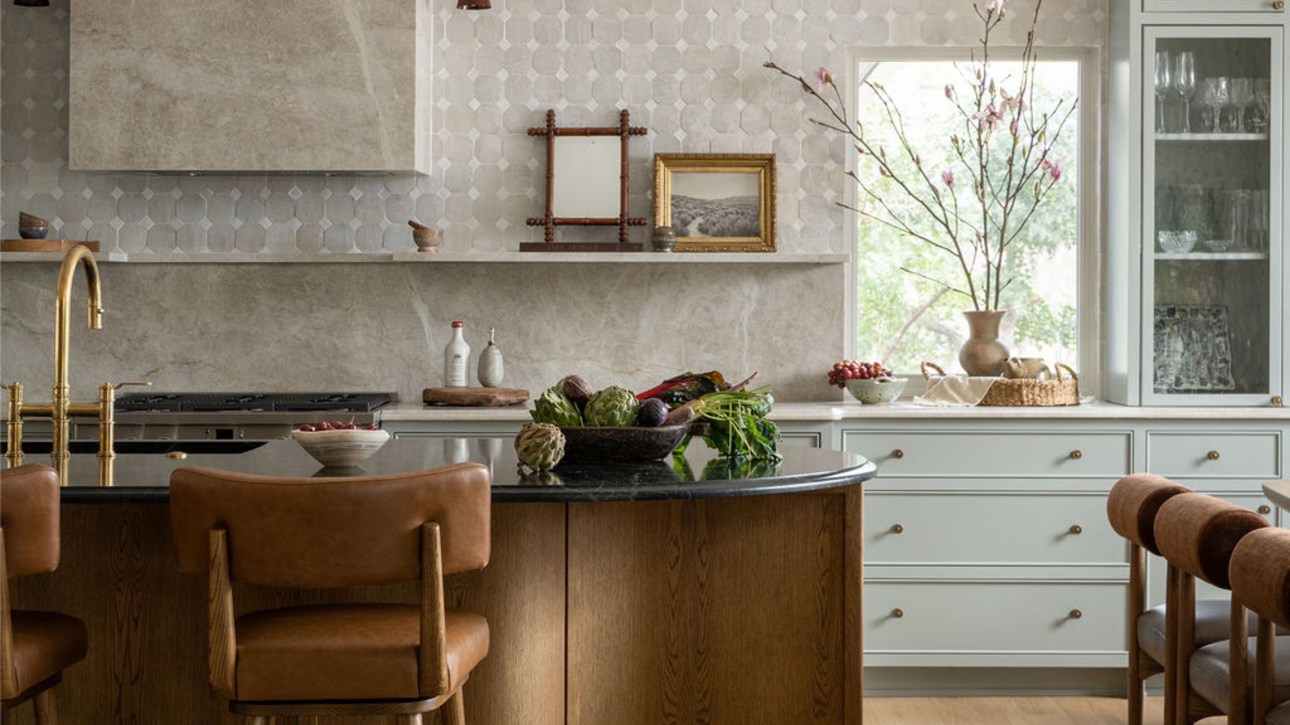 Pale blue kitchen with gray and white textured backsplash, a curved wooden island and a marble clad range hood