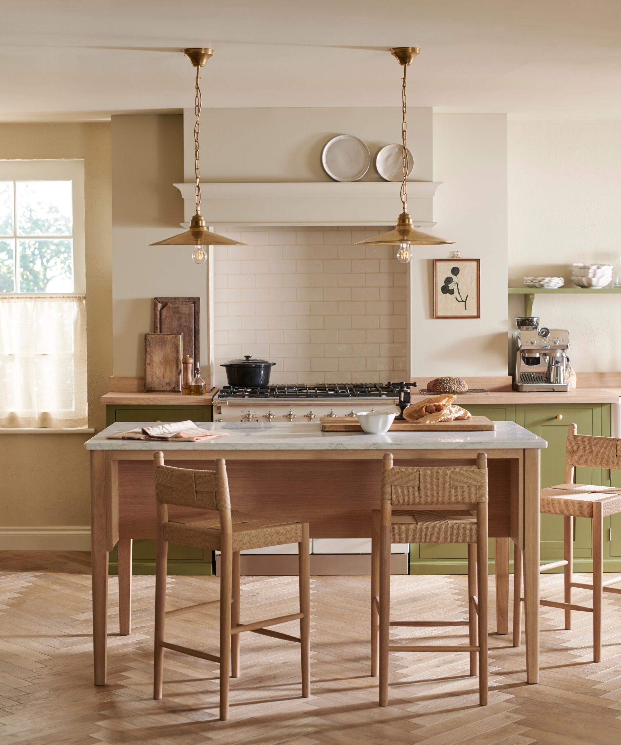 A white and green kitchen with a freestanding wooden table-style island surrounded by chairs