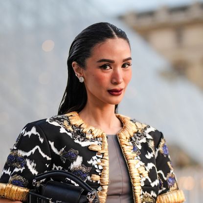 Heart Evangelista wears silver earrings, dark gray Louis Vuitton cropped top, shiny dark green Louis Vuitton leather mini skirt, black dark gray white gold pattern embroidered Louis Vuitton jacket, gold bracelets, shiny black Louis Vuitton leather bag, outside Louis Vuitton, during the Paris Fashion Week Spring/Summer 2025 on October 1, 2024 in Paris, France