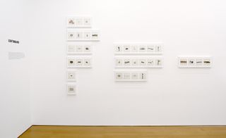Installation view of a series of small rectangular white frames with an image inside each.