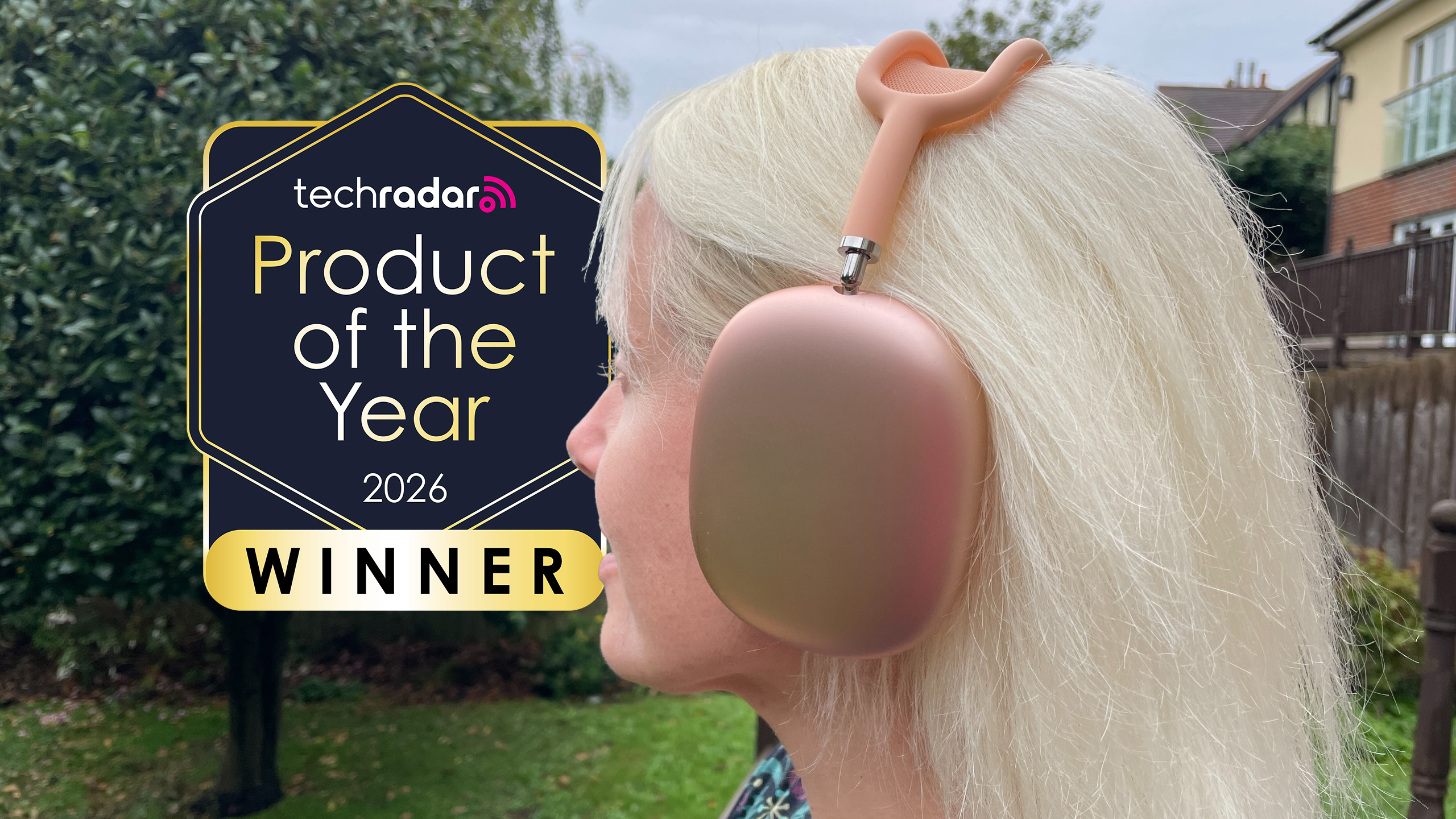AirPods Max 2 worn on a woman's head outdoors, with a sign saying "TechRadar Product of the Year 2026" winner