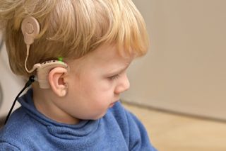 Boy wearing a hearing aid and cochlear implant