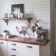 Kitchen worktop area with tiled wall and a wooden worktop, and a coffee machine on it