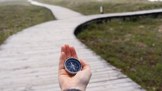 A compass in a person’s hand with a path that forks into two in the background