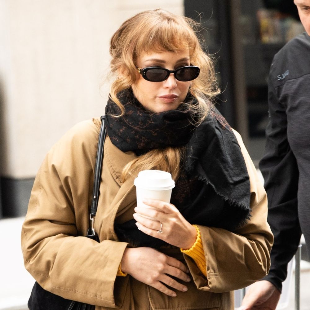 Jennifer Lawrence steps outside in New York wearing a beige trench coat with a black scarf, black sunglasses, grey jeans and Uggs.