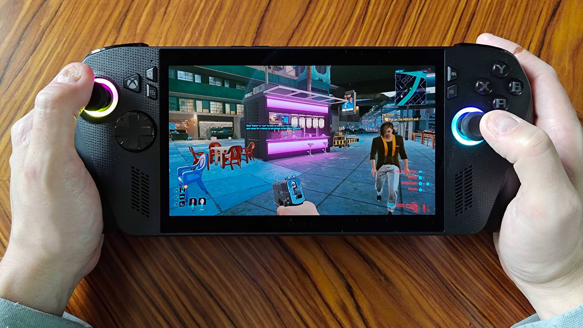 Hands holding ROG Xbox Ally X with Cyberpunk 2077 gameplay on screen.