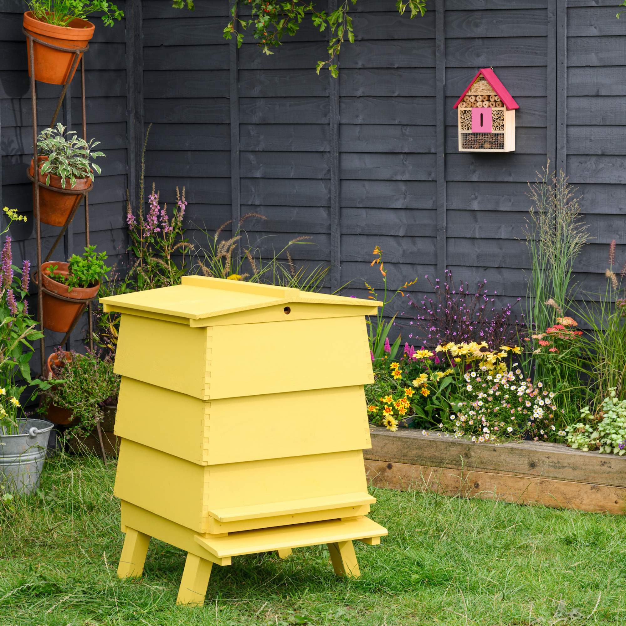 Yellow beehive in front of a black painted garden fence.