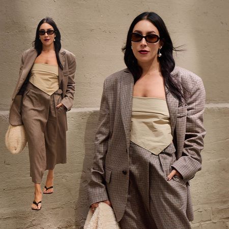 Lauren wears plaid suit, tube top, heels, and white textured handbag while walking and posing. 