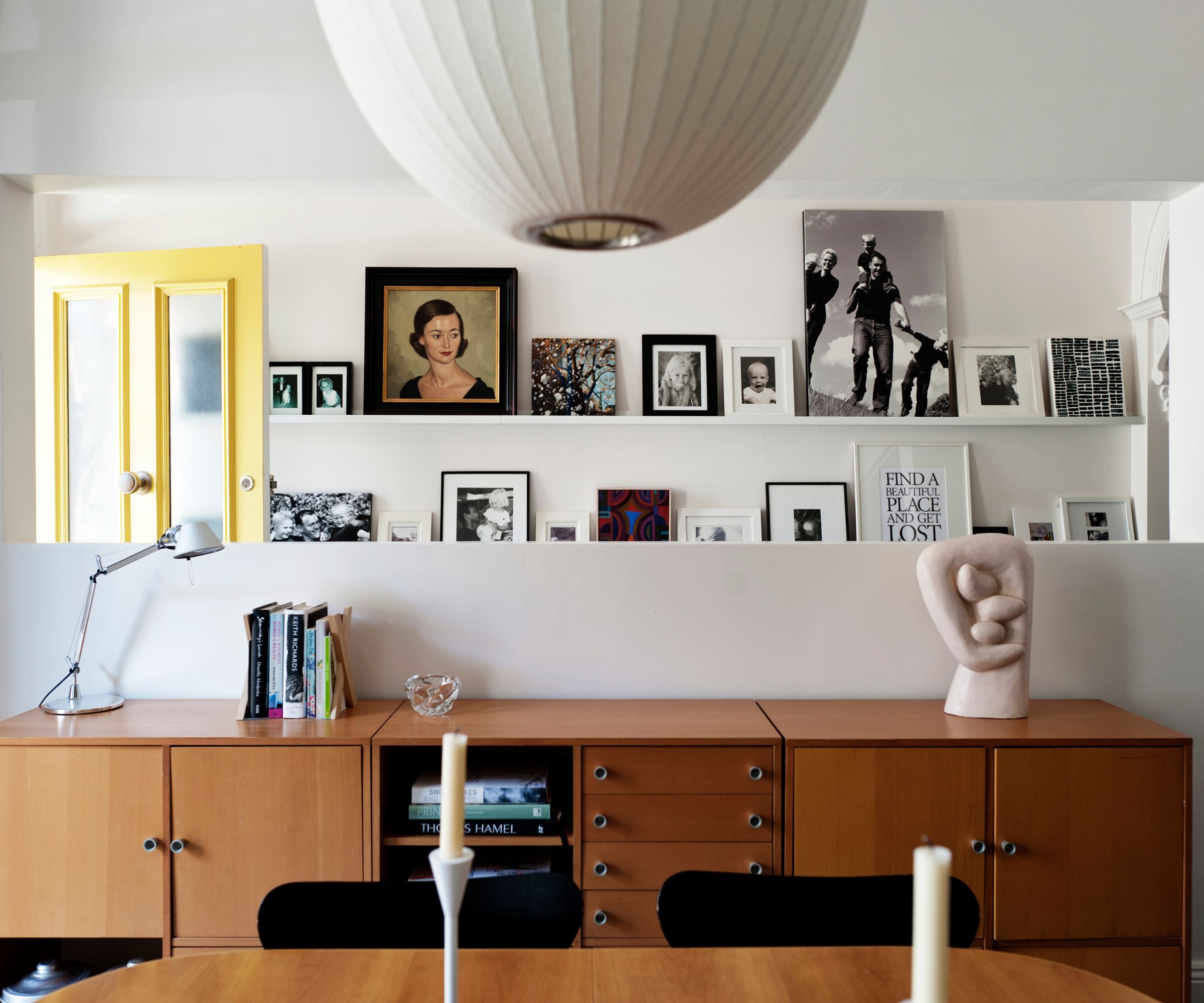 Entryway with picture ledges holding photographs and prints, midcentury console and dining table and lantern pendant light