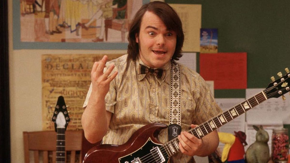 Jack Black holds a guitar in a class room 