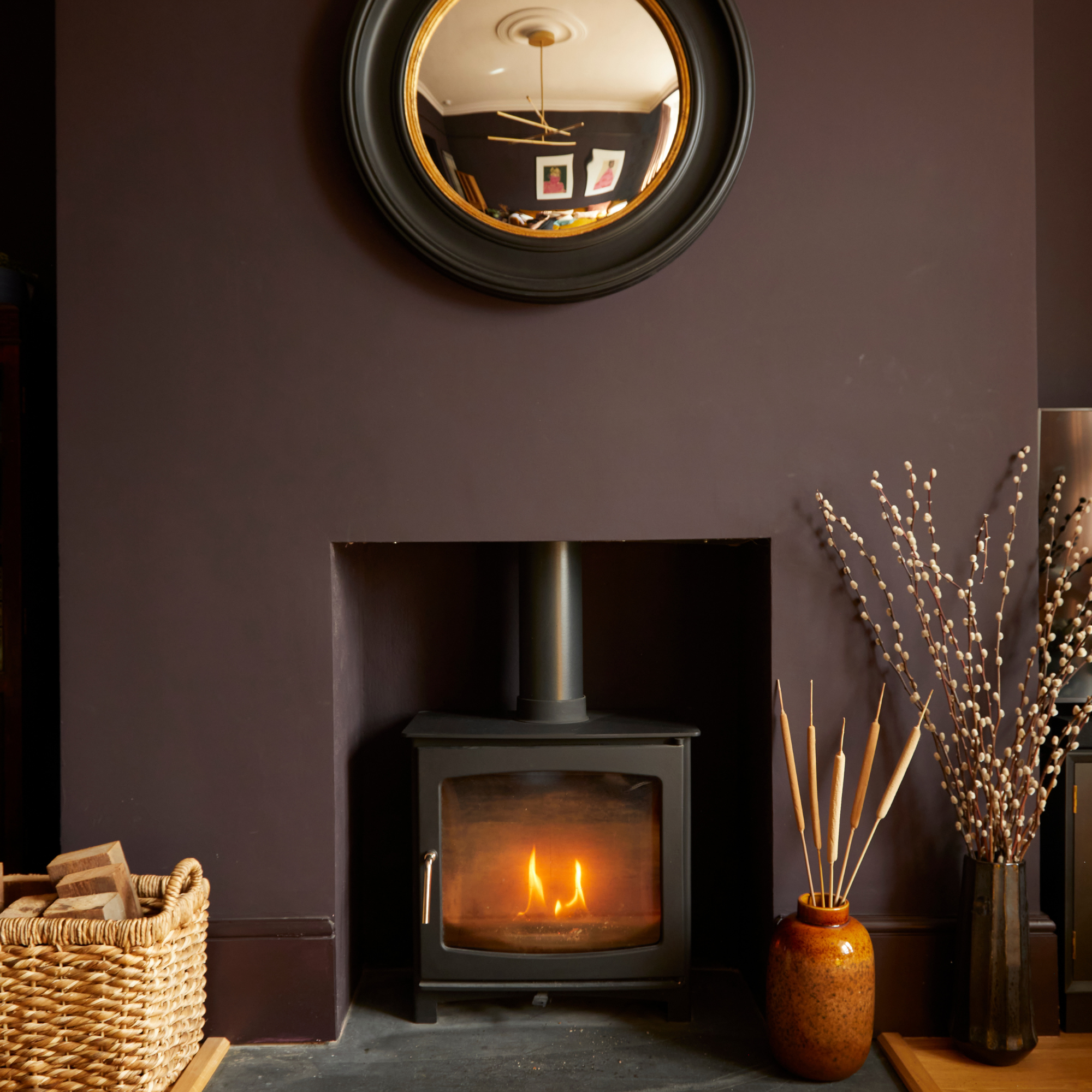 log burner, deep pruple walls and a gold and black mirror.