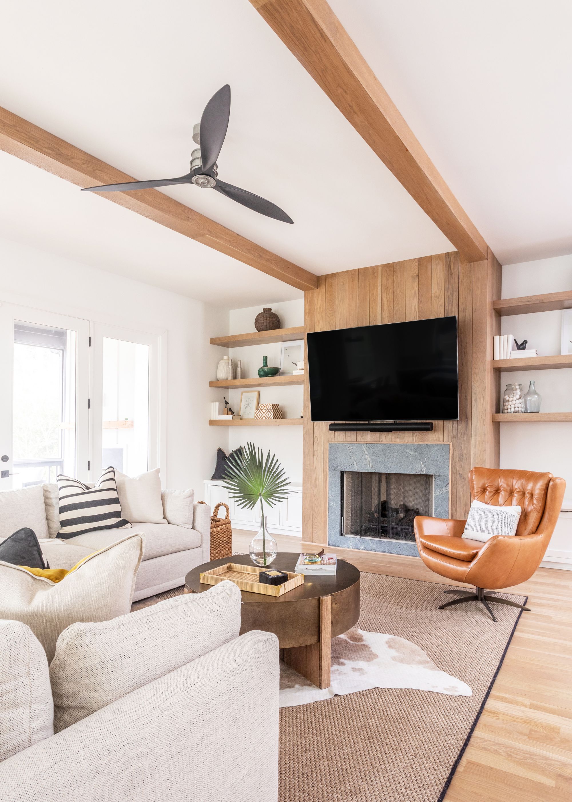 A living room with a wooden tv unit, wooden beams, and a grey fireplace