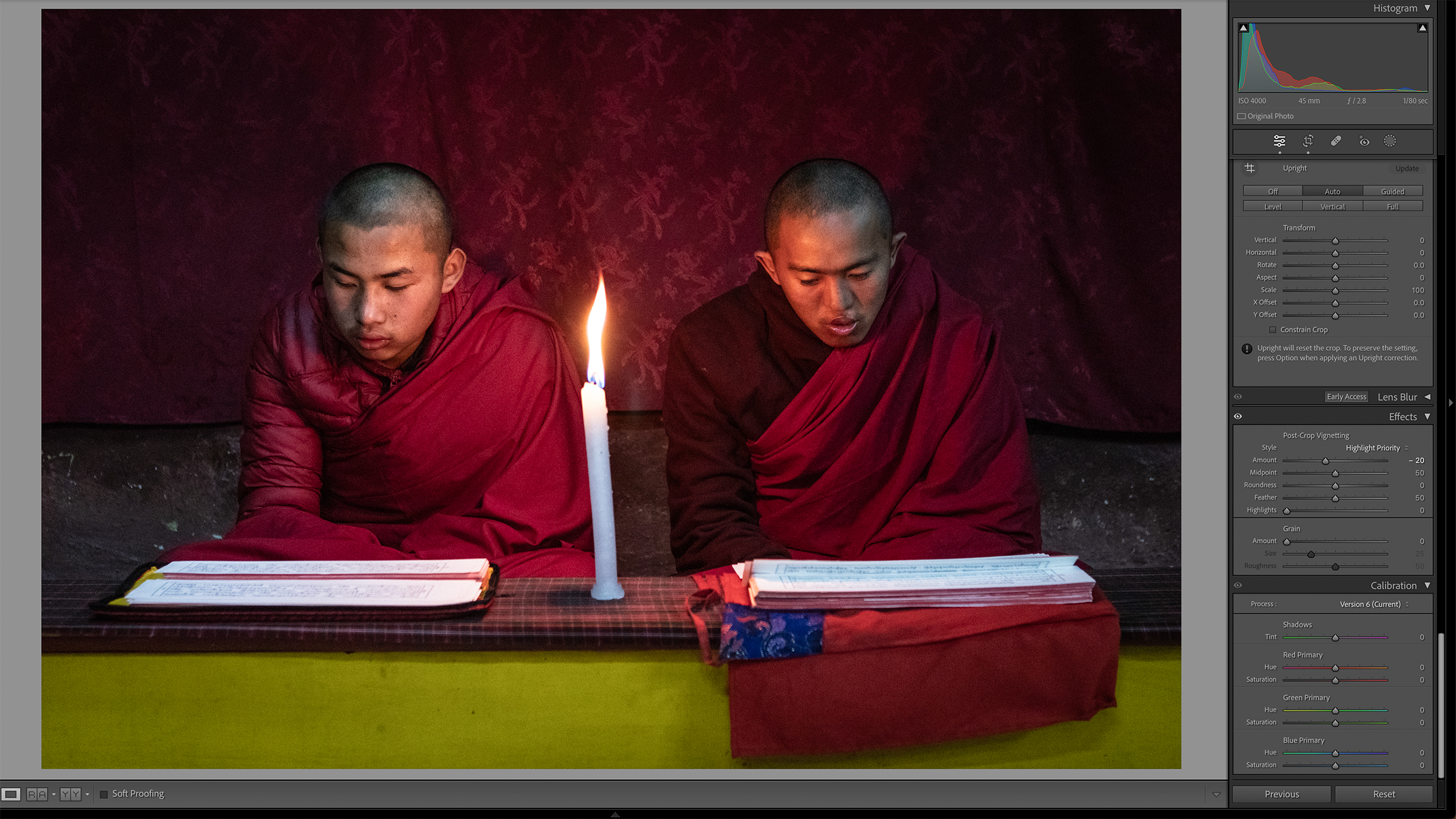 Two individuals in maroon robes are seated side by side, reading by candlelight. The dim setting conveys a calm and meditative atmosphere