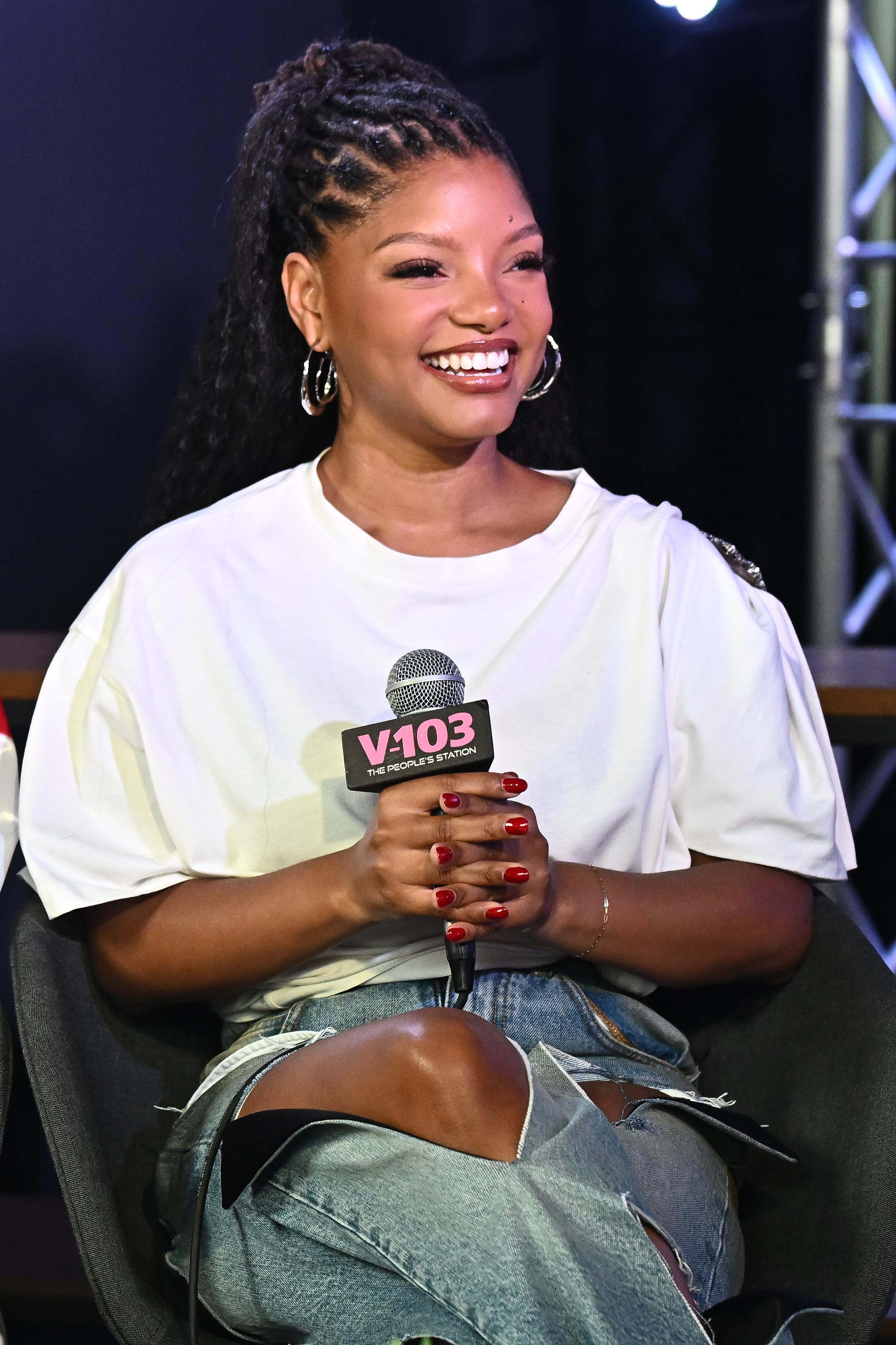 a young black woman pictured during a radio interview wearing a large white t shirt and ripped jeans