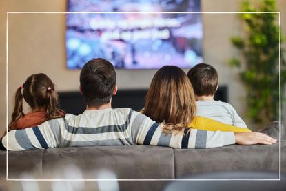 Parents and children sitting on a sofa in front of a tv that is hanging on the wall in the living room