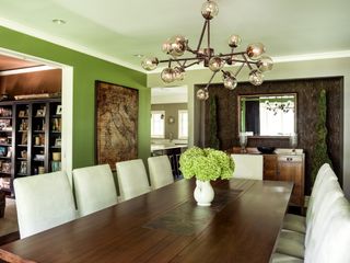 Dining room with wood table and neutral chairs, pendant lights, green walls and feature wall
