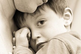 A sad crying boy cuddling his parent. 