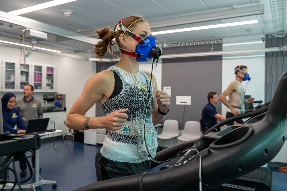 A photo of a woman wearing an oxygen mask and running on a treadmill while wearing a Samsung Galaxy Watch.