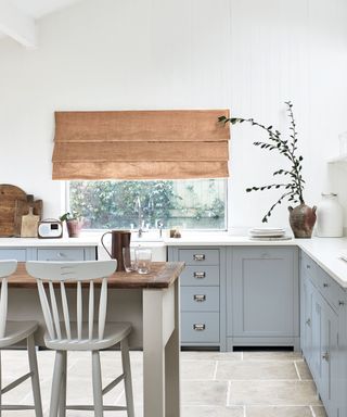 a country-style kitchen with all-white walls, white marble countertops and pale blue cabinets – with a wooden dining table and white chairs in the middle