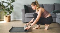 Woman rolling out yoga mat on the floor at home