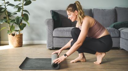 Woman rolling out yoga mat on the floor at home
