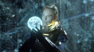 Still from the Alien movie "Prometheus." This is an image of the android David. He is a humanoid male with short blond hair. He is wearing a futuristic dark spacesuit with no helmet. He is holding a white, glowing orb in his hands. In the background you can see a grid and what looks like star constellations.