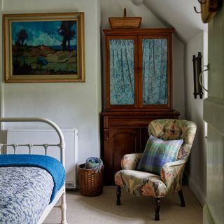 vintage armchair and laundry cupboard in a cottage bedroom