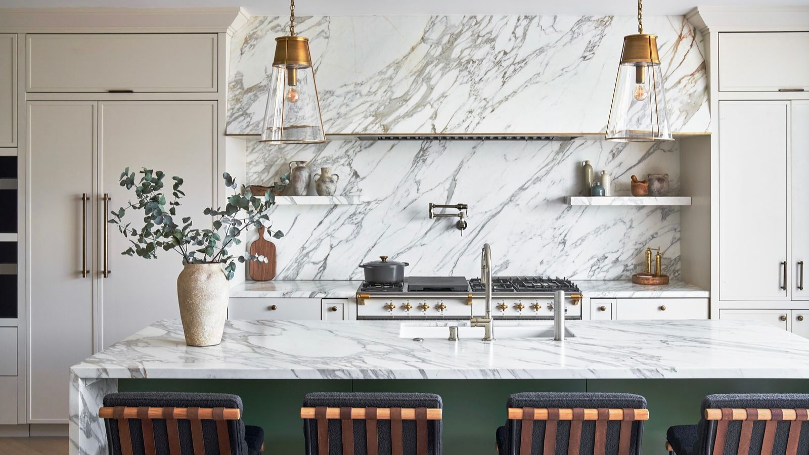 A large kitchen with white cabinets, marble countertop and backsplash, and a green island