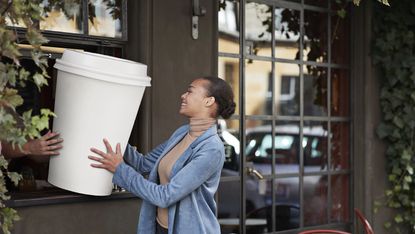 Smiling woman taking a giant coffee cup that's about 3 ft high from someone.