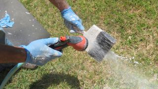 Person holding a garden hose spraying clean a paintbrush on grass background