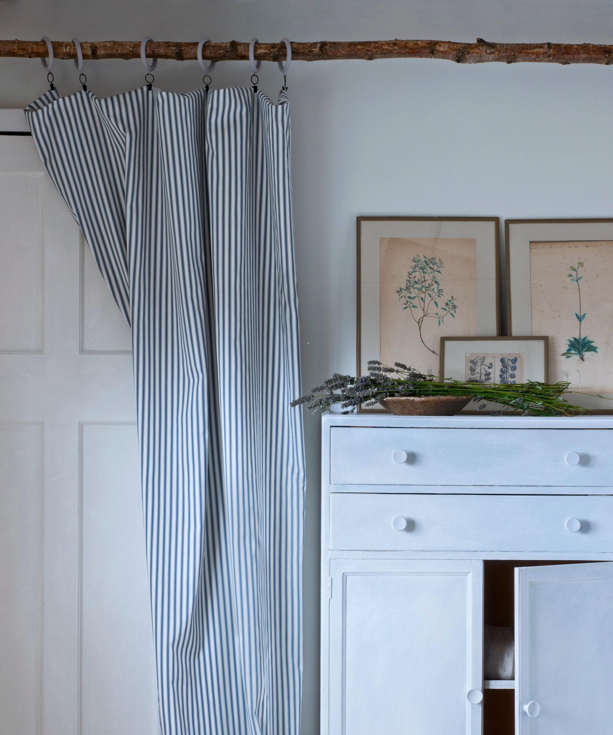Drifwood rail and blue striped curtain over pale blue cabinet with art on top