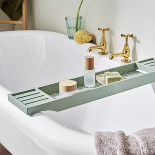 bath with green wooden bath rack with soap, bottles on it, gold taps