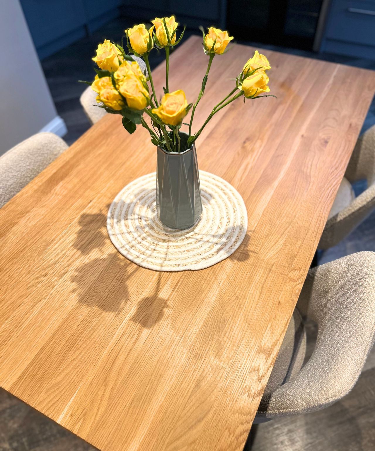 Wooden dining table with boucle chairs and yellow roses in the middle in a green vase