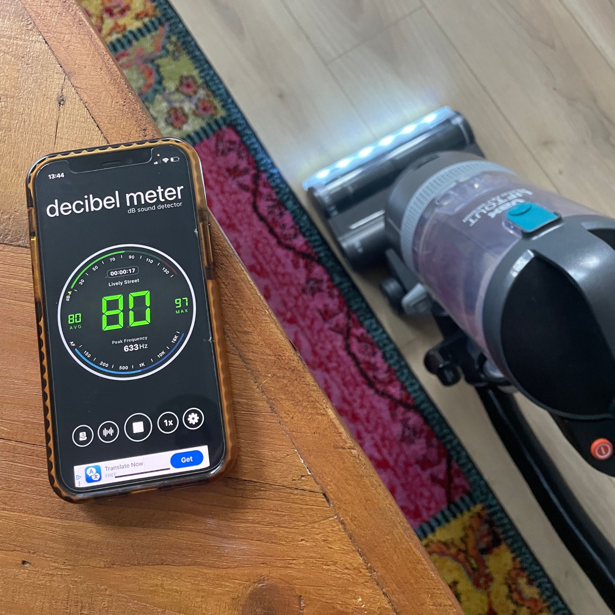 Vax LiftOut Reach Pet Design Vacuum Cleaner next to a phone on a table, which has a decibel meter app showing a reading of 80db