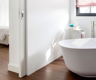 White sliding bathroom door next to white bath with wooden floor