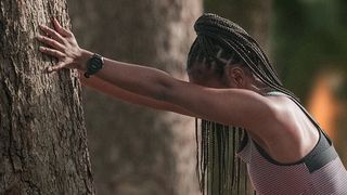 Woman stretching against tree wearing Garmin Forerunner 255 watch
