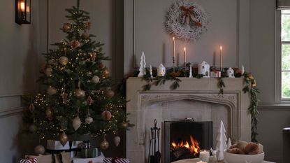 A real christmas tree lit up with fairy lights in a living room with a fireplace, decorated with a fir garland