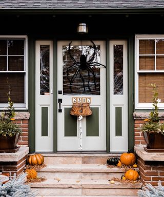 Halloween door decor ideas with a large spider over the door, with fake webbing on door and side windows, and pumpkins on steps